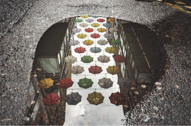 Bunte Sonnenschirme spiegeln sich in einer Regenpfütze